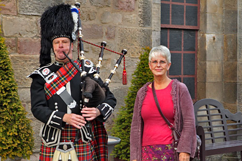 Barbara-Taste-of-Scotland Me in a skirt, posing next to a Scottish bagpiper at the entrance to "Taste of Scotland"